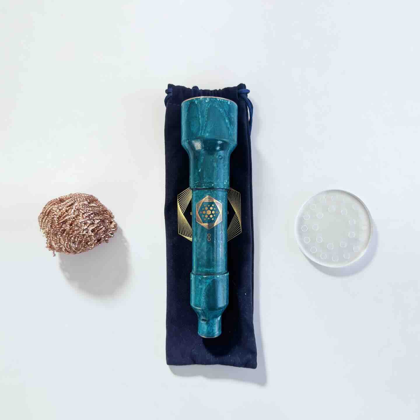 The Aqua Energizer Care Kit by The Wellness Enterprise includes a teal structured water device on a black pouch, with a metallic scrubber to the left and a clear textured disc to the right, all displayed on a white surface.