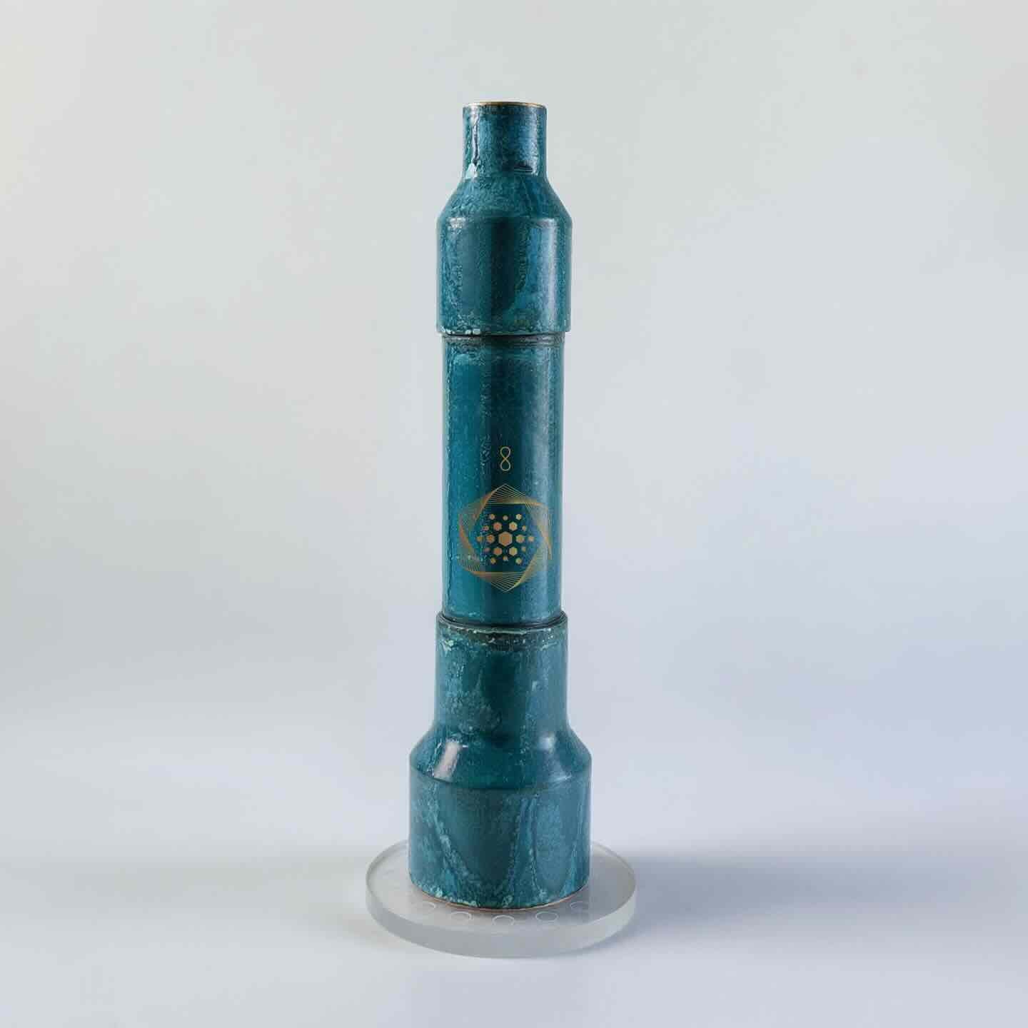 The Aqua Energizer On-the-Go Structured Water Device by Aqua Energizer is a cylindrical teal device with a stepped design, shown upright on a round clear base against a light background, designed to support cellular hydration.