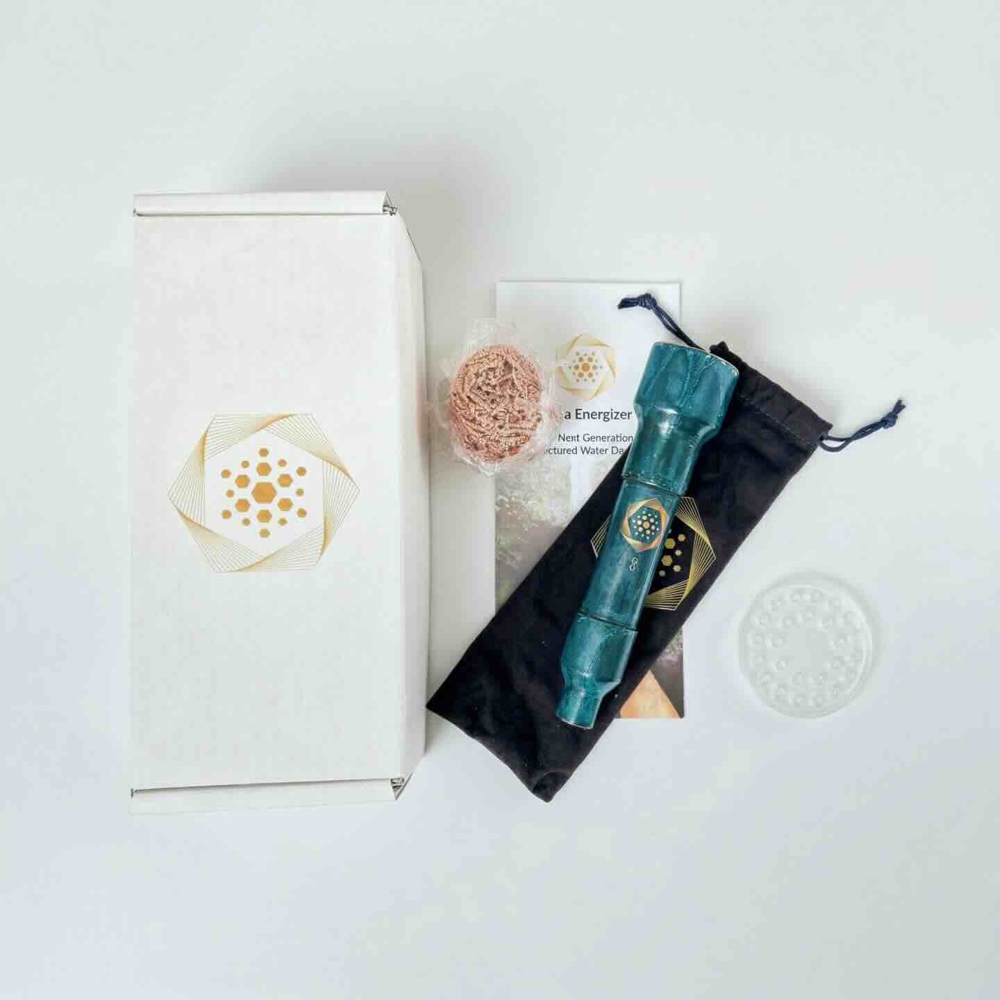 The Aqua Energizer On-the-Go Structured Water Device by Aqua Energizer is shown with a white box featuring a gold geometric logo, a turquoise wand, black pouch, loofah, clear disc, and informational card on a white surface.