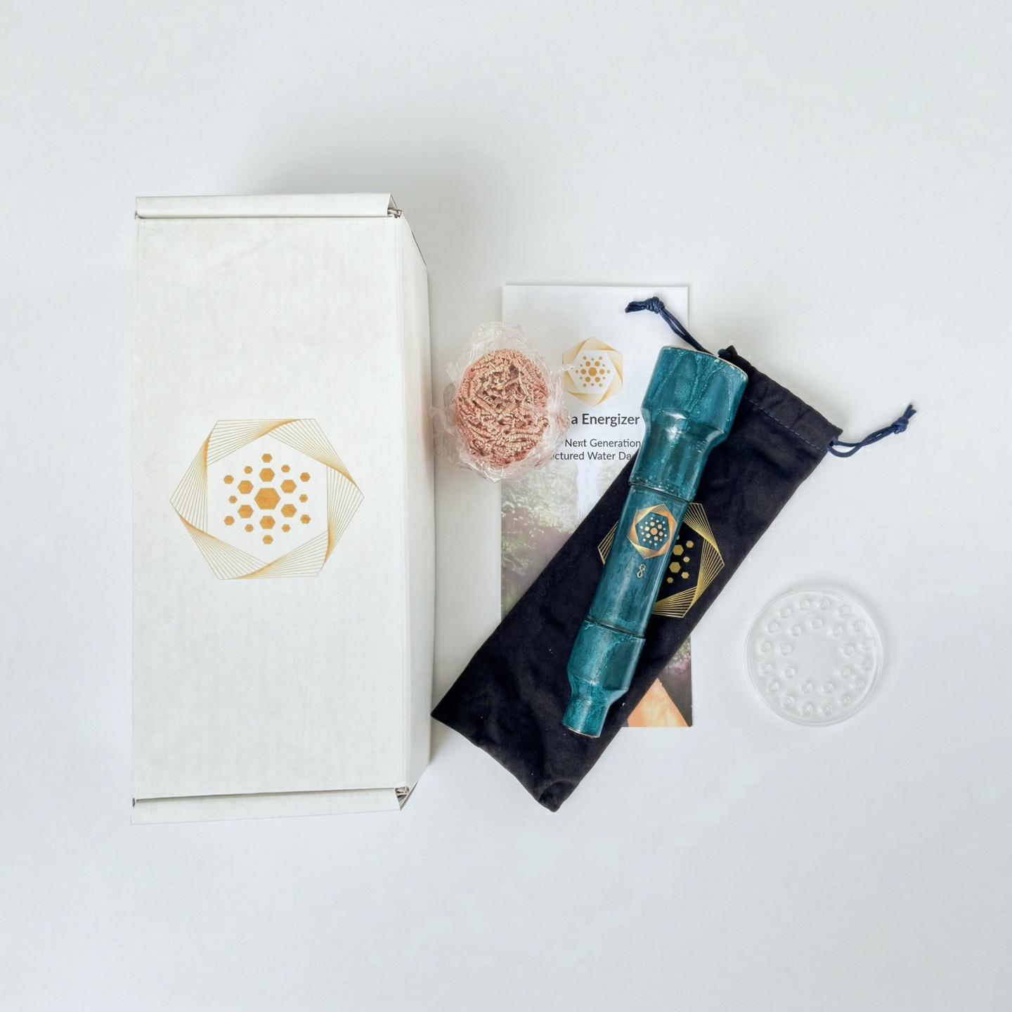 The Aqua Energizer On-the-Go Structured Water Device by Aqua Energizer, in a green cylinder and black pouch, is arranged on a white surface with its gold geometric-design box, round scrubber, clear disk, and hydration info card.