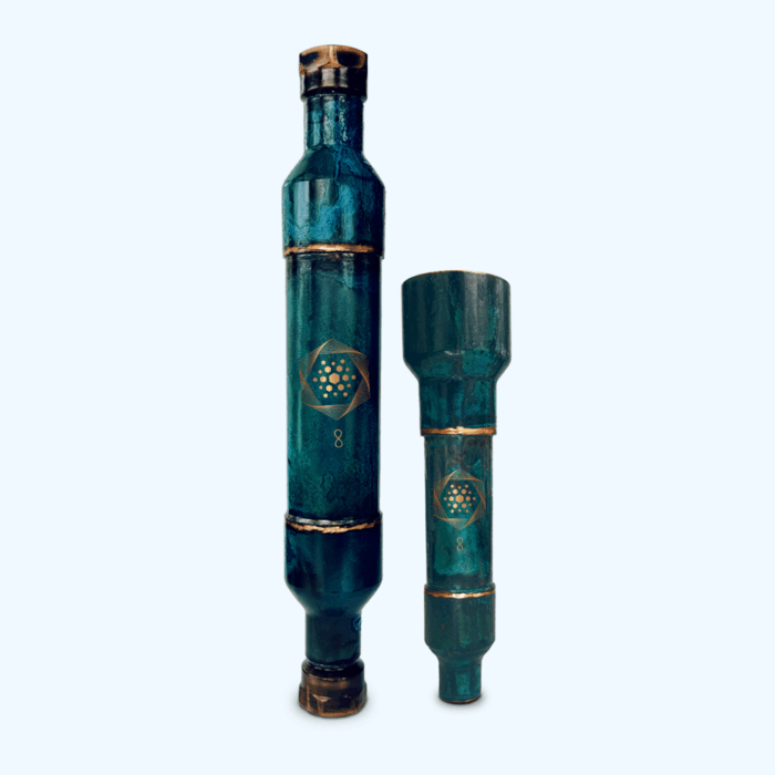 Two teal-colored cylindrical metal objects with gold accents and geometric patterns stand upright against a plain light background.