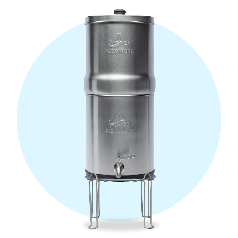 Stainless steel gravity water filter with a spigot and stand, branded "Alexapure," against a light blue circular background.