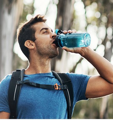 Hiker drinking water from a bottle on a forest trail