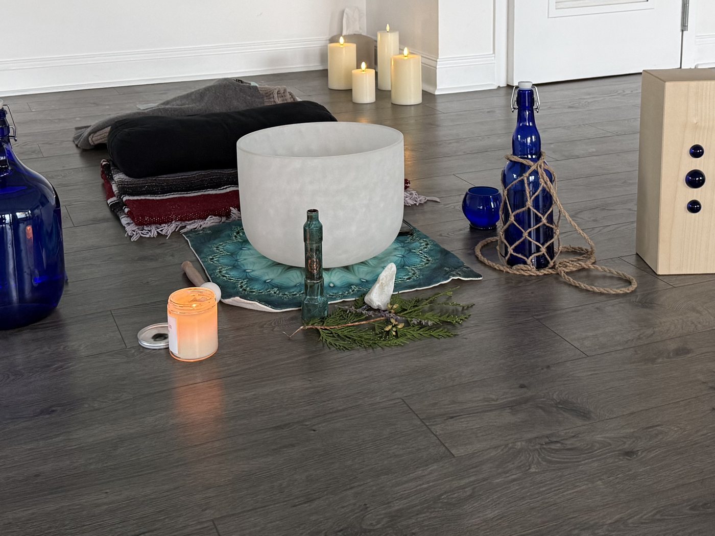 Ceremony space set with a white crystal singing bowl, cobalt blue water bottles, a candle and evergreen sprigs